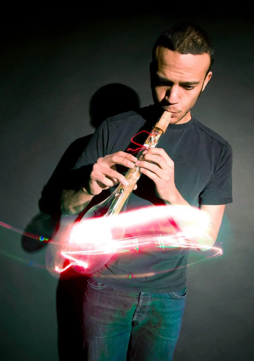 A musician playing a glassblown electronic flute, lit in red