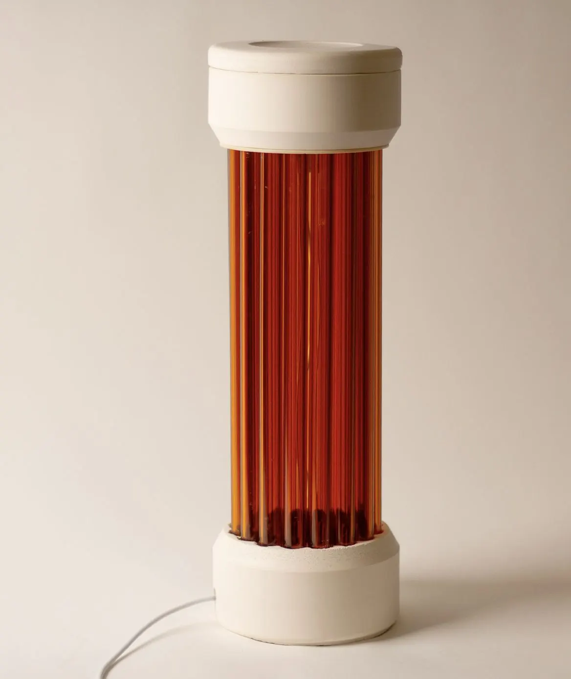 A white cylindrical lantern whose fluted core glows amber, standing on a pale base