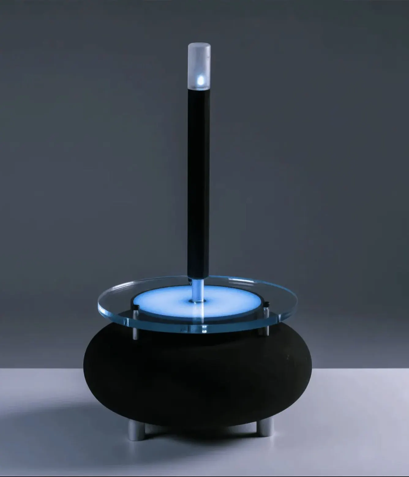 Black cylindrical object ringed with blue light, on a circular base