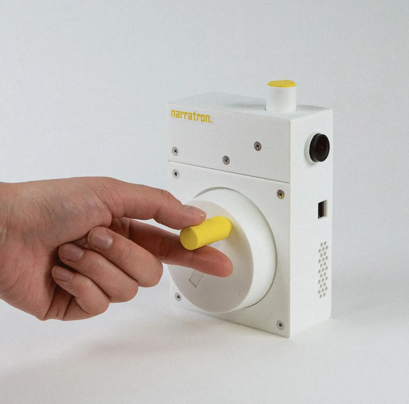 Small white cube with a yellow knob, held between two fingers